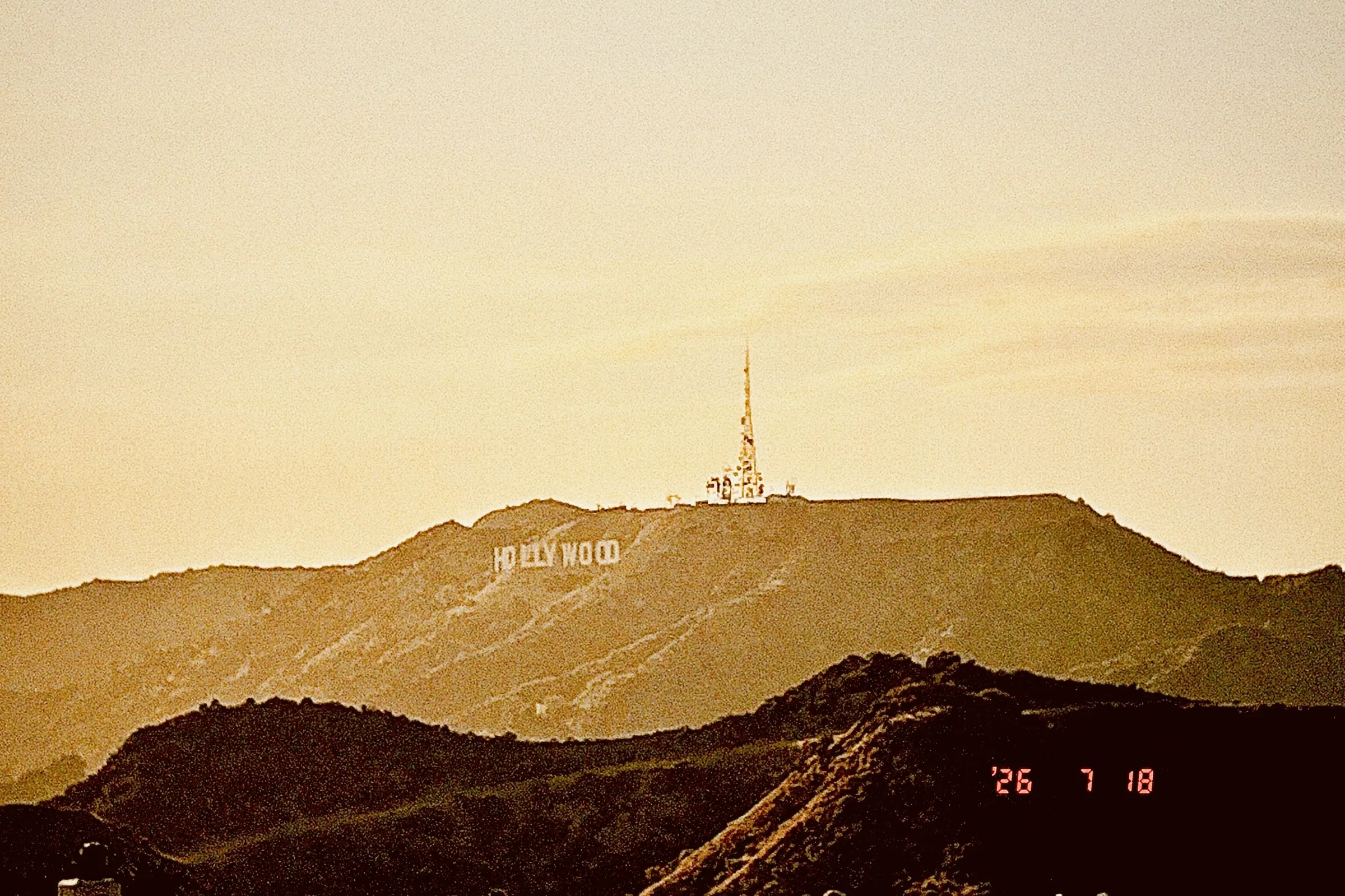 The Hollywood sign and broadcast tower on a dark ridge in warm, film-style light