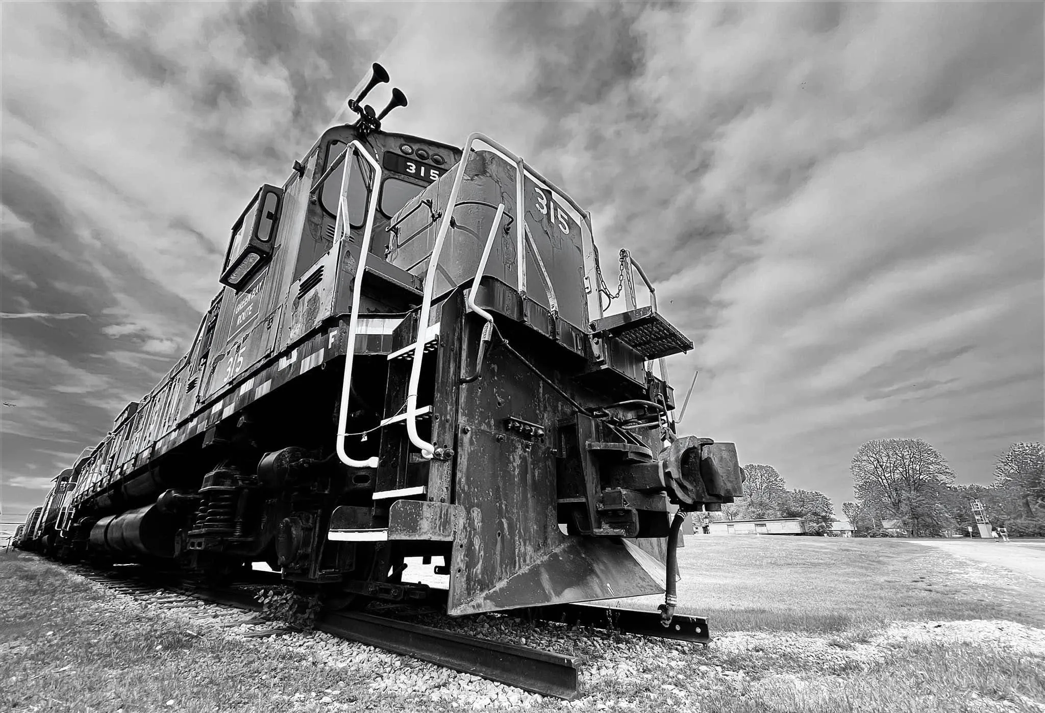 A black-and-white view of an old diesel locomotive parked on a short stretch of track under a dramatic cloudy sky