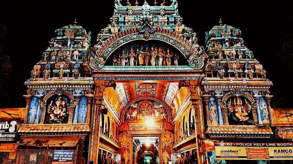 The ornate, brightly painted entrance gate of a South Indian temple, lit up at night